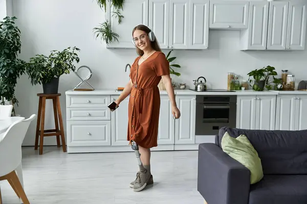 Жінка в коричневій сукні танцює на кухні з навушниками на. — Stock Photo