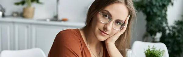 Eine Frau mit Brille und einem sanften Lächeln sitzt in einem sonnendurchfluteten Raum. — Stockfoto