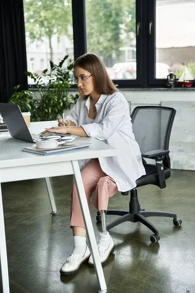 Une femme avec une jambe prothétique travaille sur son ordinateur portable à un bureau. — Photo de stock