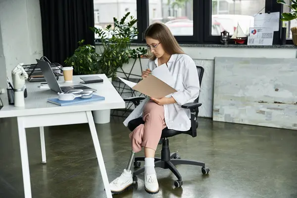 A woman with a prosthetic leg sits at her desk, reviewing documents. — Stock Photo