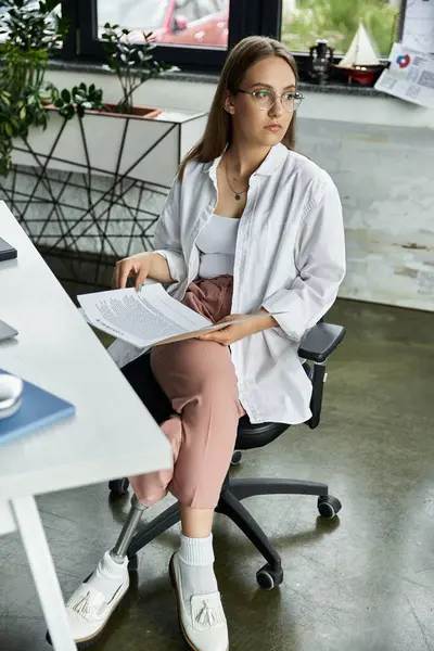 Woman with prosthetic leg reads document in office chair, gazing aside — Stock Photo