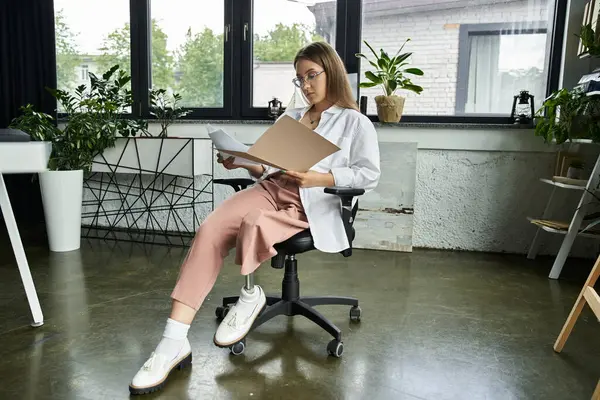 A young woman with a prosthetic leg sits in an office chair reviewing documents. — Stock Photo
