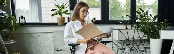 Woman in white shirt reviews documents in office chair as sunlight streams through window — Stock Photo
