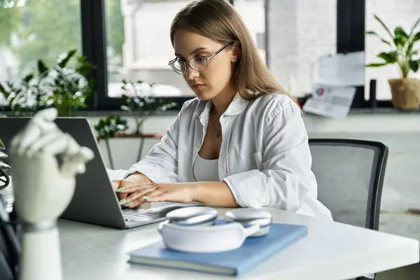 A woman sits at a desk typing on a laptop. — Stock Photo