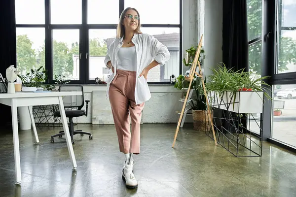 A woman in a white shirt and pink pants stands confidently in a modern office setting. — Stock Photo