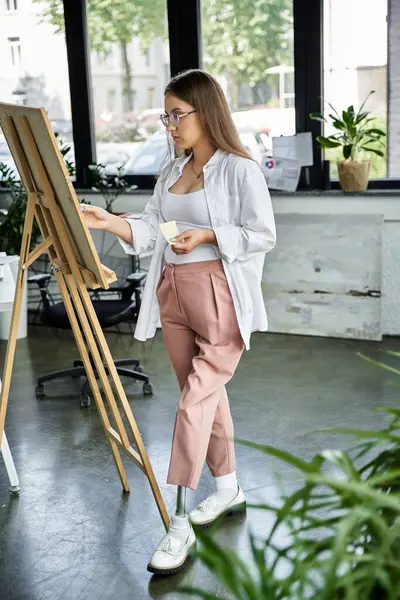 A young woman with a prosthetic leg examines her canvas while standing in a studio. — Stock Photo