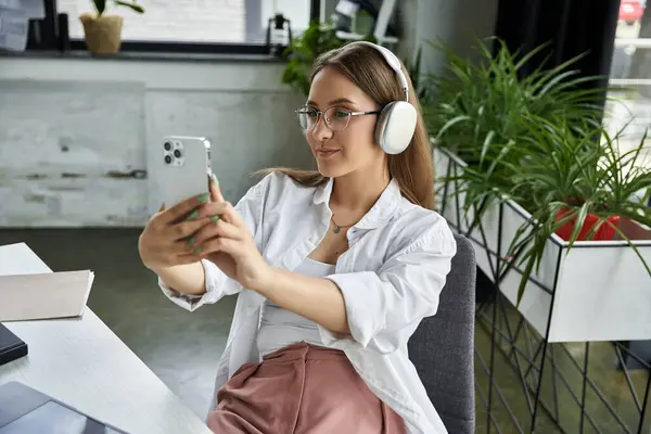 A woman takes a selfie with her phone while wearing headphones. — Stock Photo