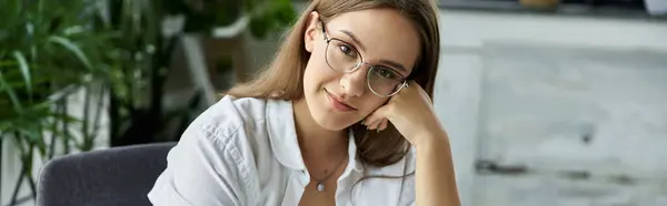 A woman with glasses rests her chin on her hand, looking confidently at the camera. — Stock Photo