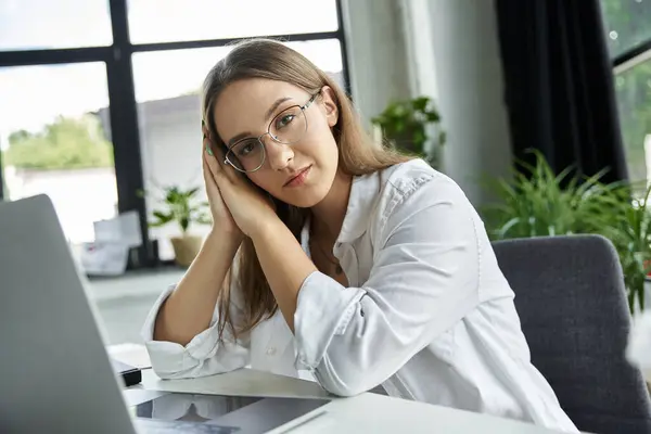 Mujer con gafas se sienta en el escritorio, las manos en la cara en la contemplación tranquila - foto de stock