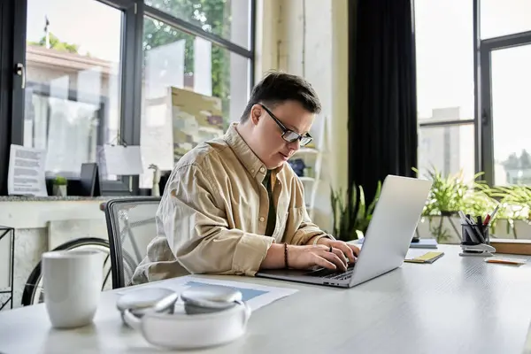 A young man with Down syndrome works on a laptop at a desk. — Stock Photo