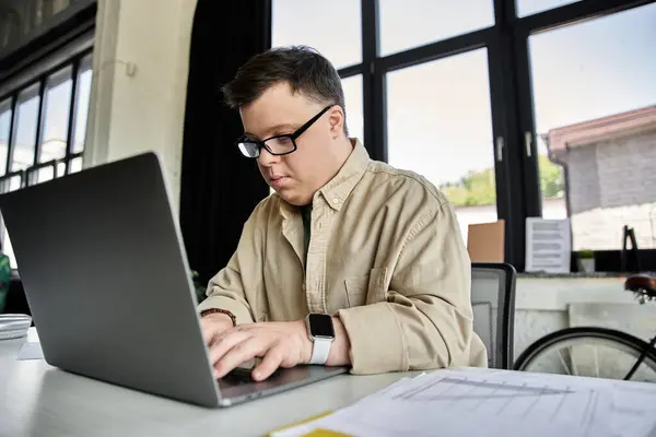A young man with Down syndrome focuses intently on his work while typing on a laptop. — Stock Photo