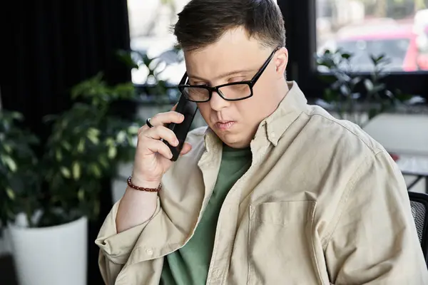 Jovem com síndrome de Down em óculos, camisa bege, faz telefonema dentro de casa — Fotografia de Stock