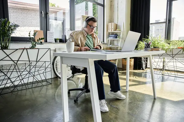 A young man with Down syndrome sits at a desk in an office, working on a laptop. — Stock Photo
