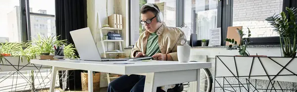 Un jeune homme trisomique est assis à un bureau, travaillant sur son ordinateur portable. — Photo de stock