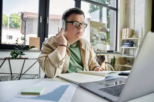 A young man with Down syndrome working on laptop with headphones and notebook — Stock Photo