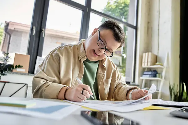 A young man with Down syndrome sits at a desk, working on paperwork. — Stock Photo