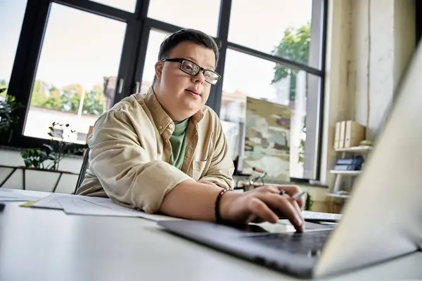 A young man with Down syndrome focuses on his work, typing on a laptop. — Stock Photo