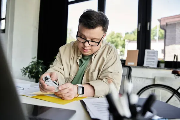 A young man with Down syndrome with glasses sits at a desk, carefully reviewing documents. — Stock Photo