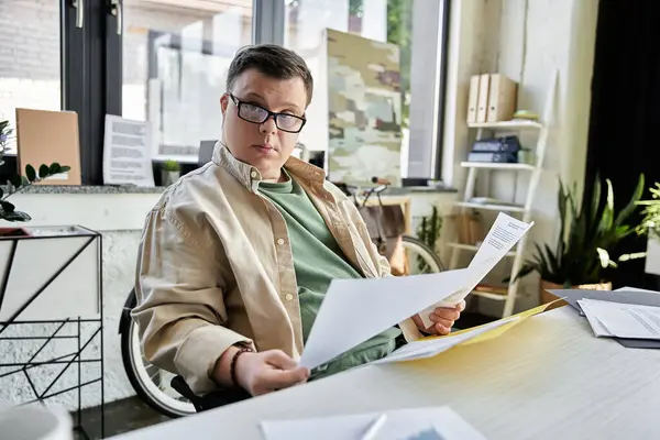 Un jeune homme trisomique s'assoit à son bureau, examinant des documents. — Photo de stock