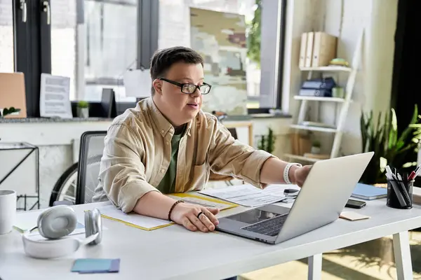 Un jeune homme trisomique travaille avec diligence sur son ordinateur portable dans un espace de bureau moderne. — Photo de stock