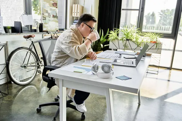 A young man with Down syndrome sits at his desk, taking a break from work to enjoy a cup of coffee. — Stock Photo