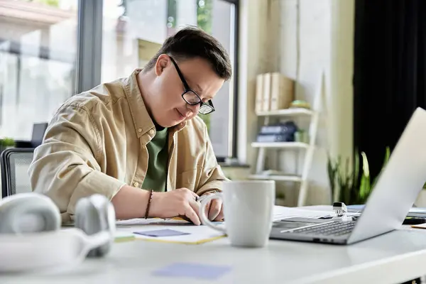 Un jeune homme trisomique travaille à un bureau, concentré sur sa tâche. — Photo de stock