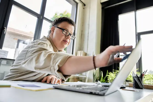 Ein junger Mann mit Down-Syndrom benutzt einen Laptop in einem gut beleuchteten Büroraum. — Stockfoto