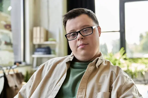 A man with Down syndrome, wearing beige shirt and glasses, looks at camera in a room — Stock Photo