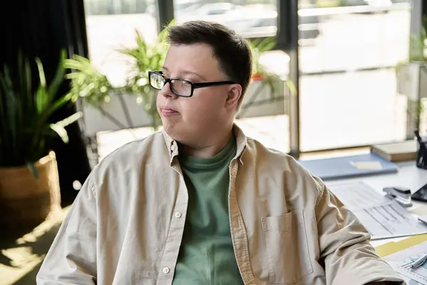 Молодий чоловік з синдромом Дауна сидить за столом, задумливо дивлячись в бік. — стокове фото