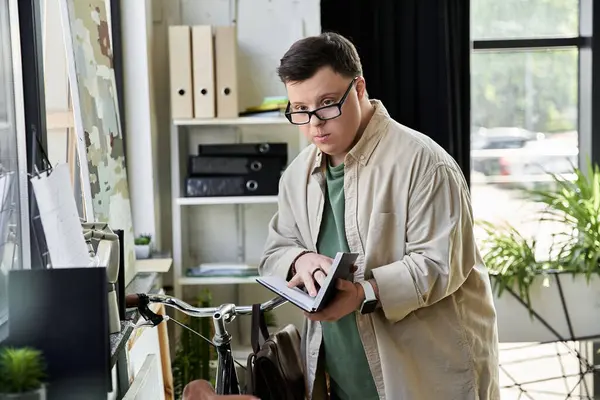 Un jeune homme trisomique dans une chemise de couleur claire lit un livre tout en se tenant dans un bureau moderne. — Photo de stock