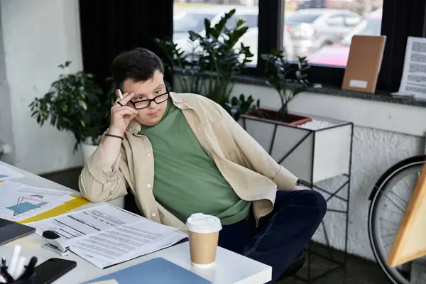 Un homme trisomique passe en revue la paperasse à son bureau avec un café à proximité — Photo de stock