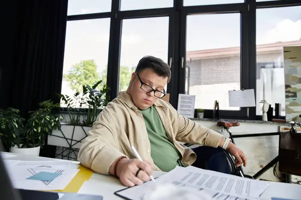 A young man with Down syndrome sits at a desk, focused on filling out paperwork. — Stock Photo