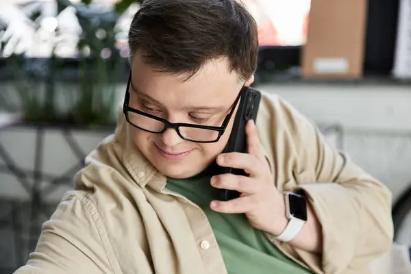 Young man with Down syndrome, glasses, brown shirt smiles while on phone — Stock Photo