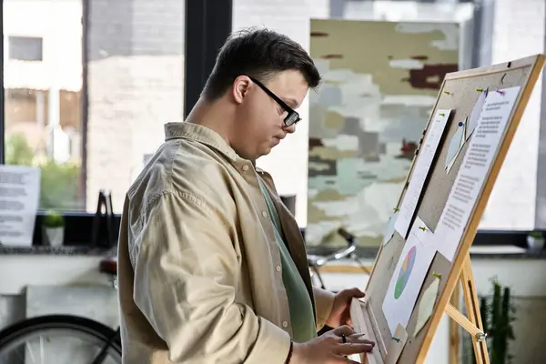 A young man with Down syndrome stands near a whiteboard, reviewing a presentation. — Stock Photo