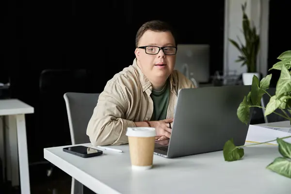 Ein junger Mann mit Down-Syndrom arbeitet an seinem Laptop am Schreibtisch. — Stockfoto