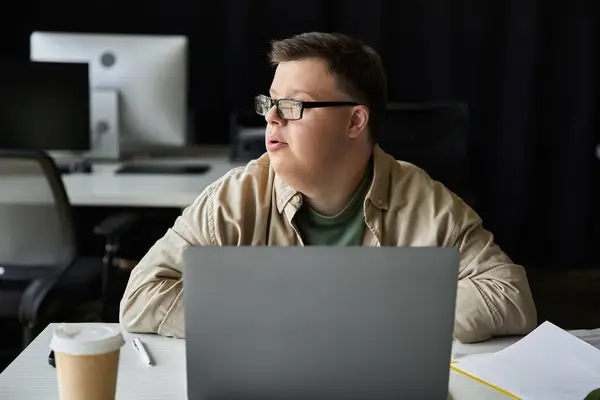 Ein junger Mann mit Down-Syndrom arbeitet intensiv an seinem Laptop im Büro. — Stockfoto