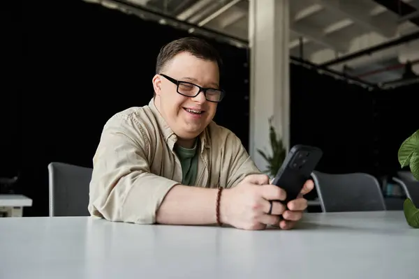 A young man with Down syndrome smiles while using his phone at a table. — Stock Photo