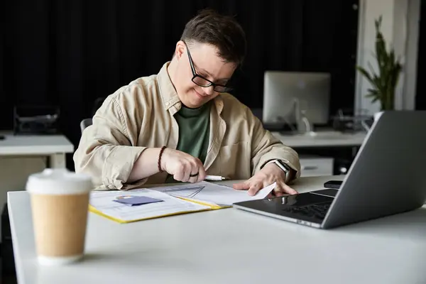 Hombre joven con síndrome de Down trabaja duro en el escritorio, portátil y café cerca — Stock Photo