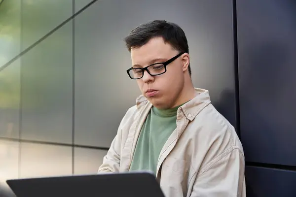 Un hombre con síndrome de Down se sienta afuera, trabajando en su portátil. - foto de stock