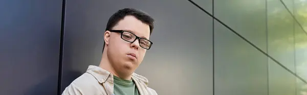 A young man with Down syndrome stands outside, leaning against a wall. — Stock Photo