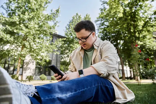 A man with Down syndrome relaxes on the grass, enjoying a moment on his phone. — Stock Photo