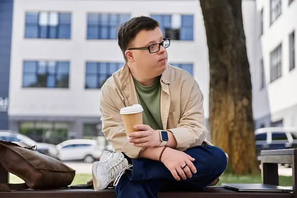 A man with Down syndrome sits on a bench, enjoying a cup of coffee. — Stock Photo