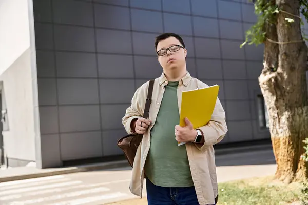 A man with Down syndrome walks outside a building, carrying a folder and a bag. — Stock Photo