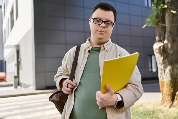 A man with Down syndrome holds a yellow folder while walking outside a building. — Stock Photo