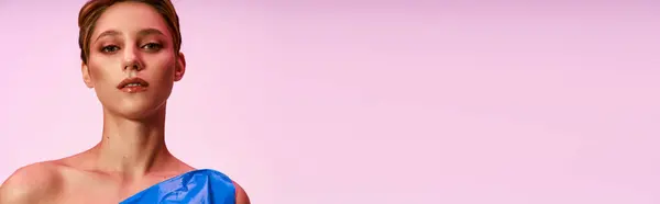 Uma mulher em um vestido azul olha diretamente para a câmera contra um fundo rosa. — Fotografia de Stock