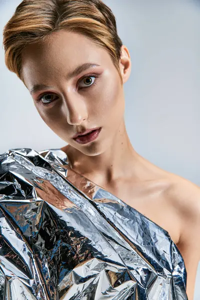 A woman with a short haircut poses while wearing a silver foil dress. — Stock Photo