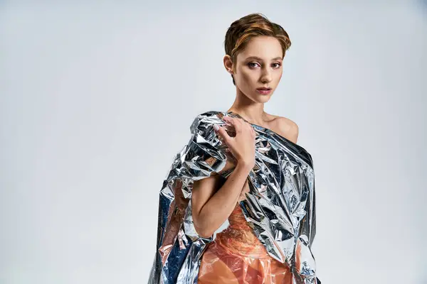 A woman in a silver, sustainable fashion design stands against a white backdrop. — Stock Photo