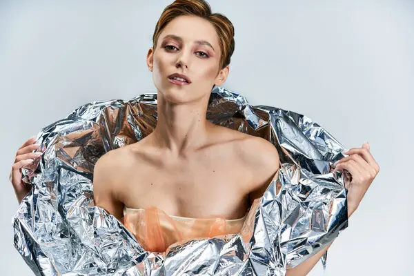 A woman in a silver foil garment, posing with a confident and alluring gaze. — Stock Photo