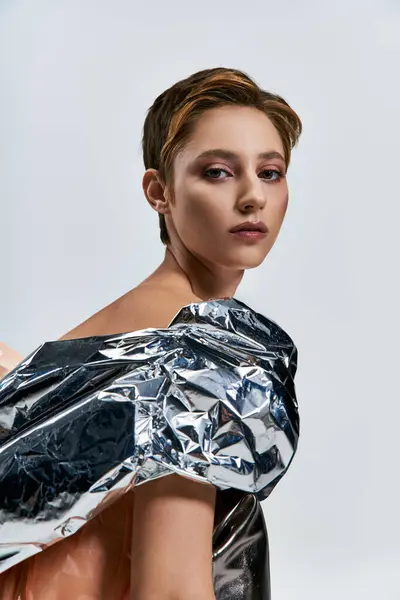 A woman in a silver, sustainable fashion garment gazes intently at the camera. — Stock Photo