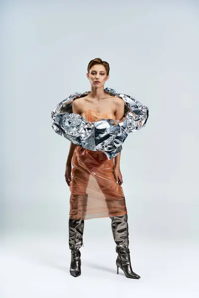 A woman poses in a studio, wearing a silver foil top and a plastic skirt. — Stock Photo